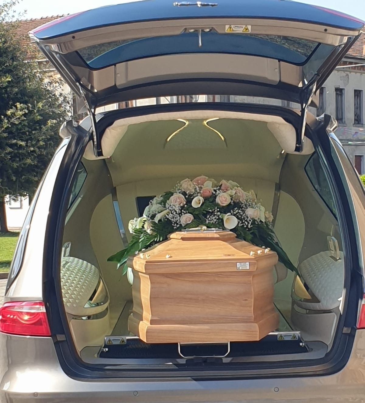 Person in dark suit standing beside a polished wooden casket at a graveside funeral