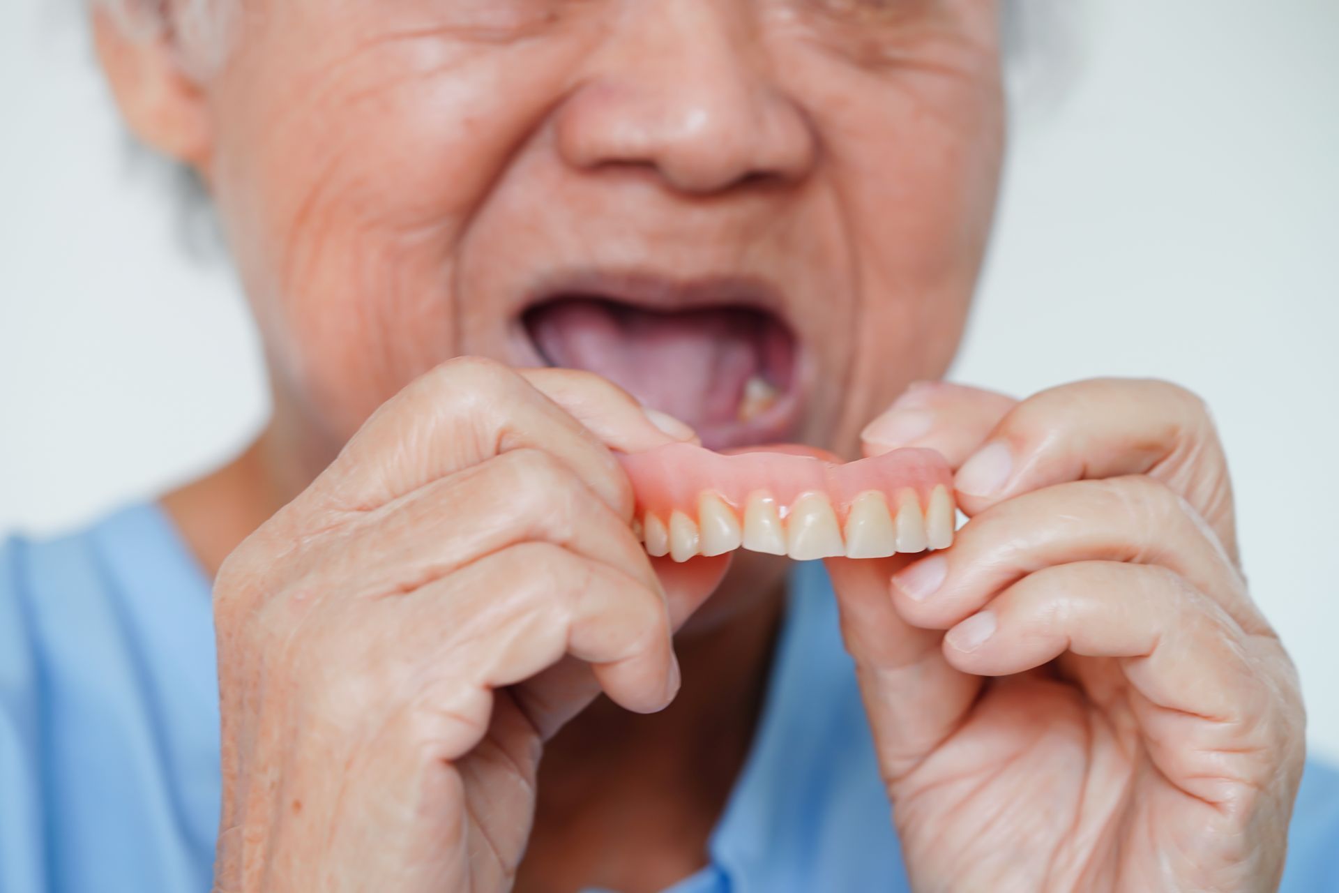 Une personne portant une chemise bleue tenant un dentier supérieur devant sa bouche.