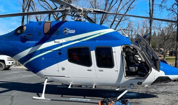 Blue and white helicopter parked on the ground with its side door open in a snowy outdoor setting