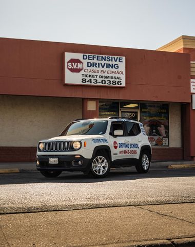 White Jeep parked outside a Defensive Driving School storefront with a sign overhead.