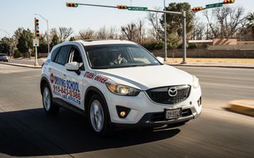 White SUV with company graphics driving through an intersection on a sunny street