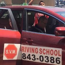 Red driving school car with phone number and driver visible inside during a lesson