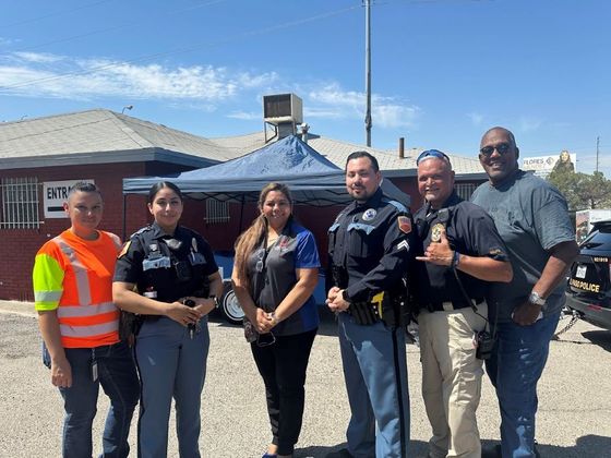 Six uniformed officers and one safety worker standing together outdoors on a sunny street.