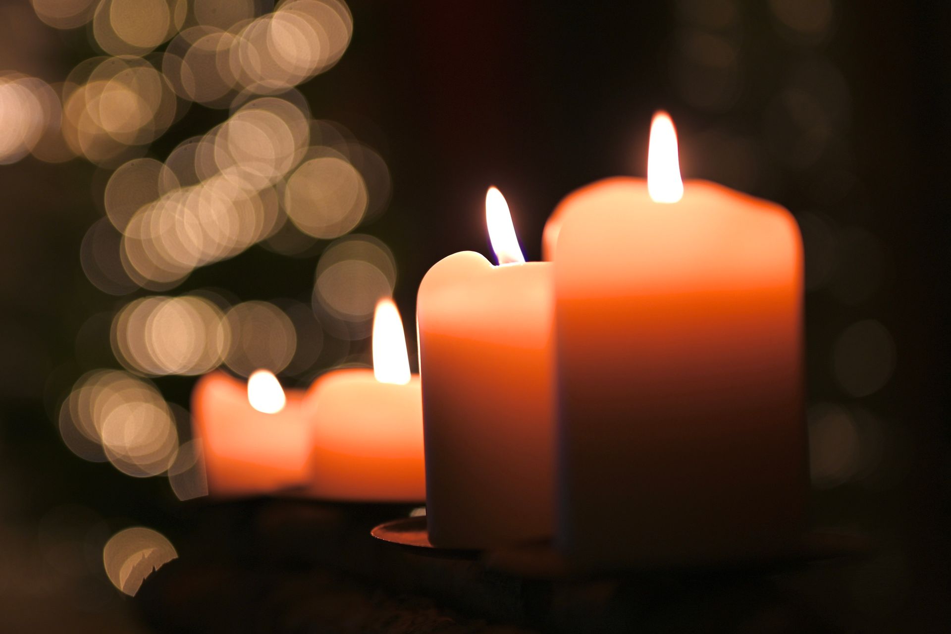 Tre candele accese su un portacandele con luci di Natale sullo sfondo