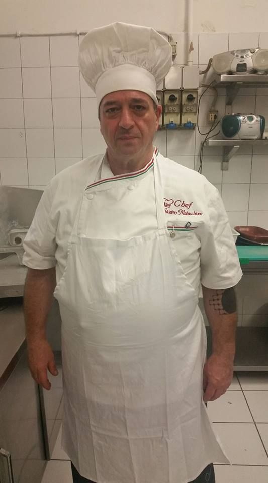 Un uomo con cappello da cuoco e grembiule è in piedi in cucina.