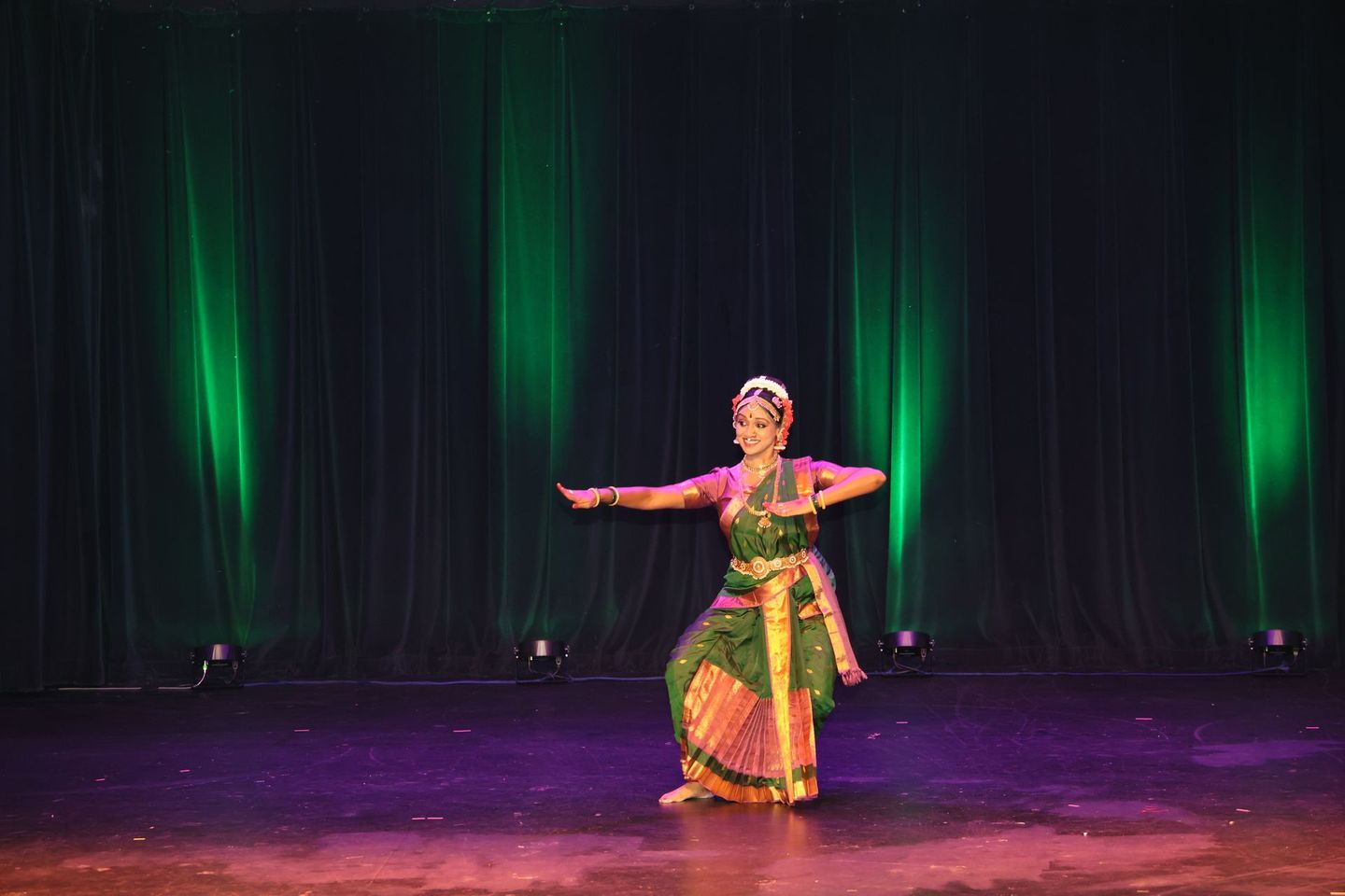 Kuchipudi dancer in green and orange traditional costume performing on a dark stage with green lights