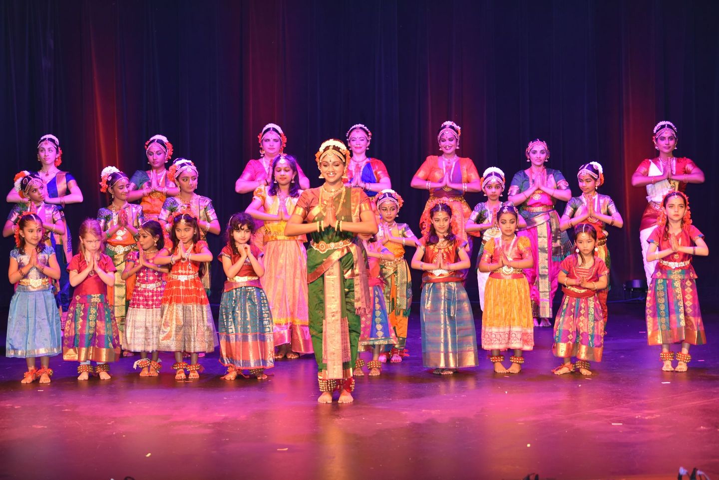 Group of Kuchipudi dancers in colorful costumes performing on a stage with purple lighting