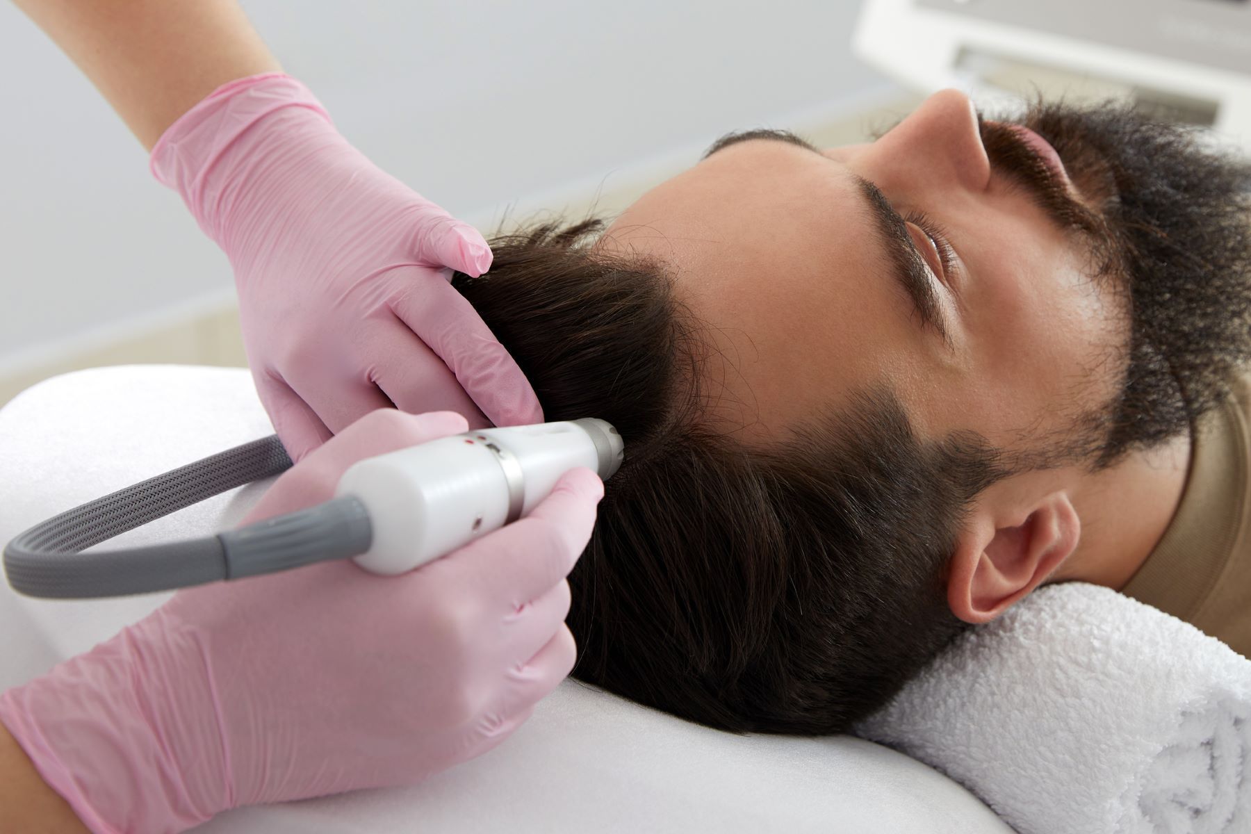 A person receiving scalp treatment with a handheld device, gloved hands in frame.