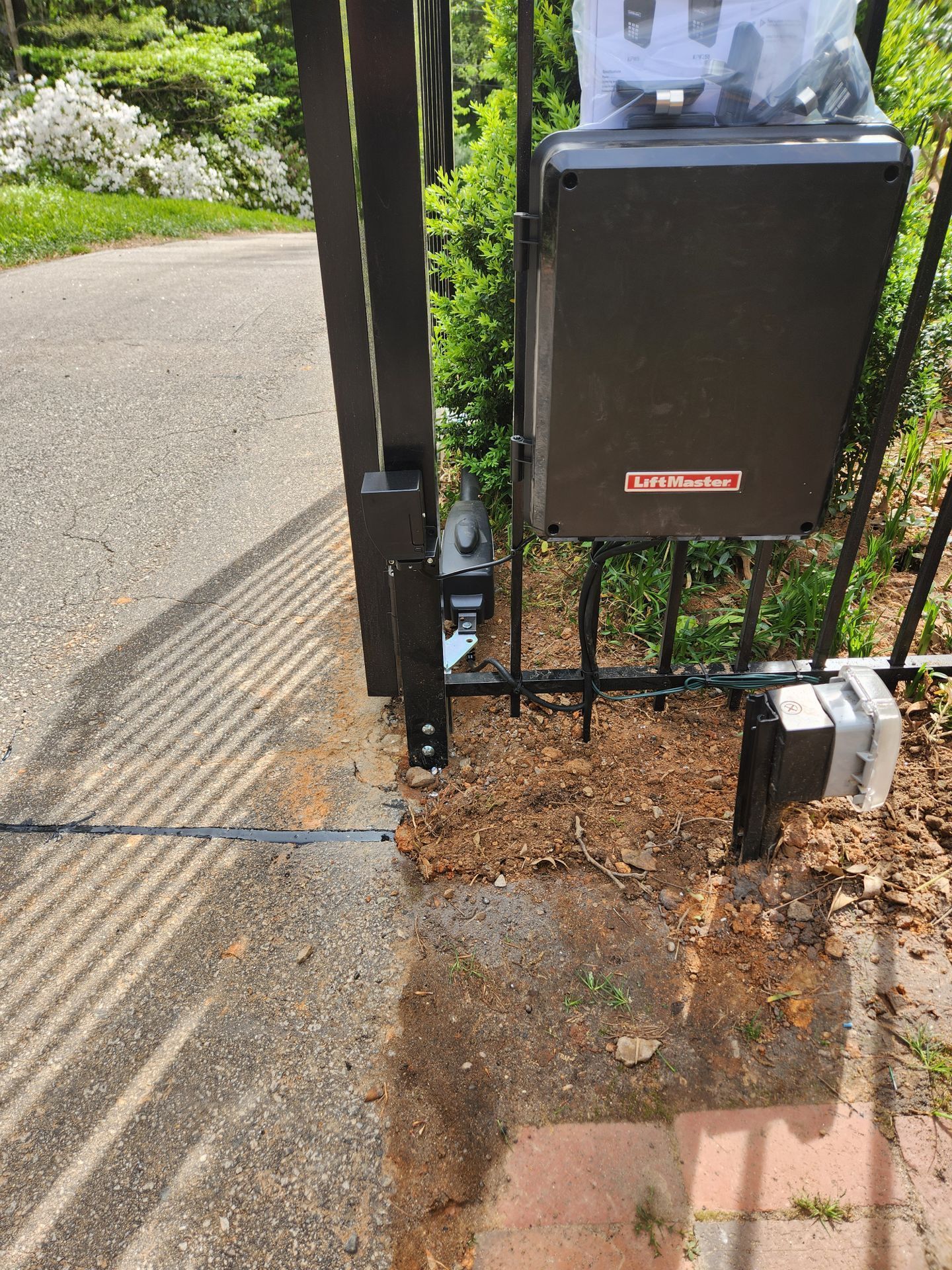 Damaged driveway gate beside a paved path, with dirt and debris piled at the base