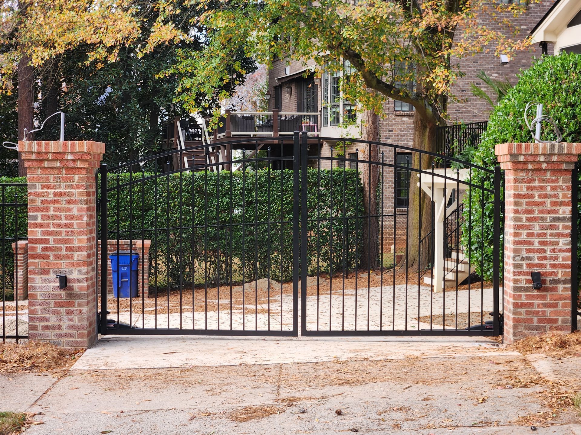 Brick pillars with a black metal gate at the entrance to a tree-lined residential property.