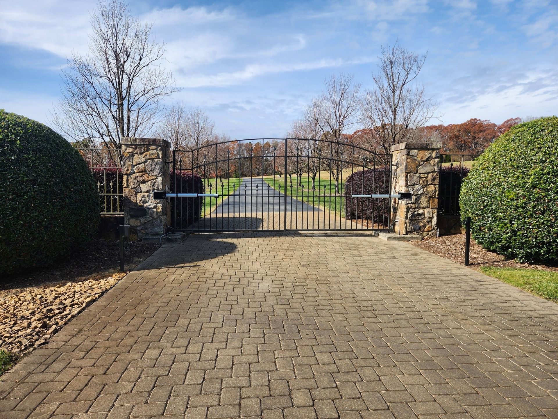Brick driveway leading to a gated garden entrance with stone pillars and trimmed hedges