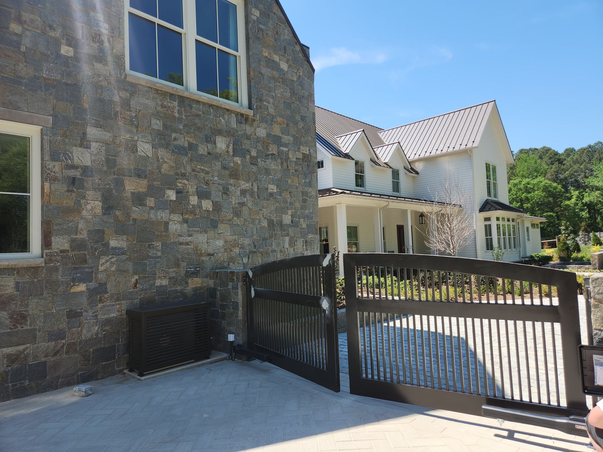 Stone house with white trim beside a driveway and black gate on a sunny day