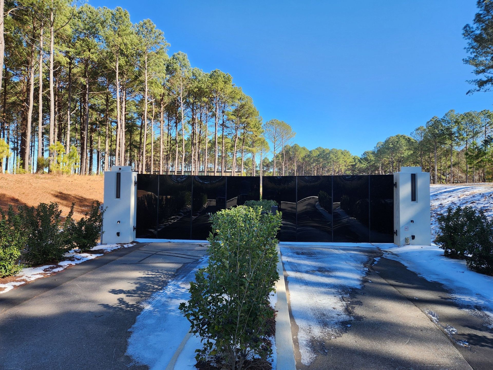 Tree-lined driveway leading to a dark gated entrance under a blue sky