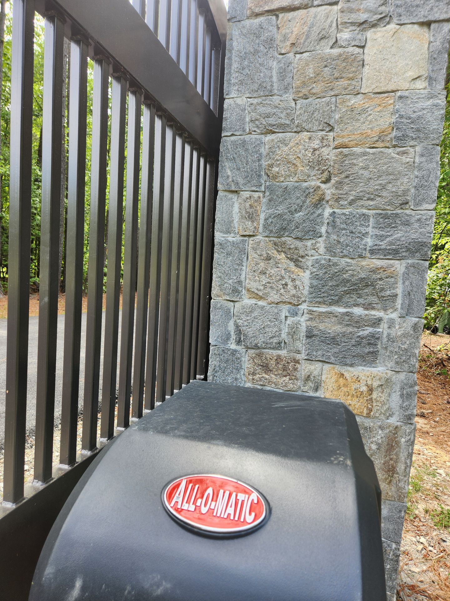 Black grill with red logo beside a stone wall and metal fence outdoors