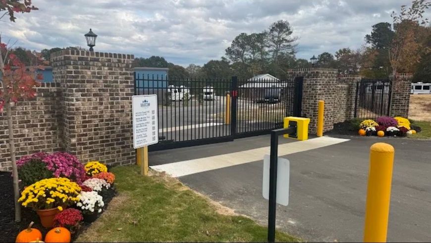 Brick gate entrance with black iron gates, yellow bollards, and flower beds along the driveway