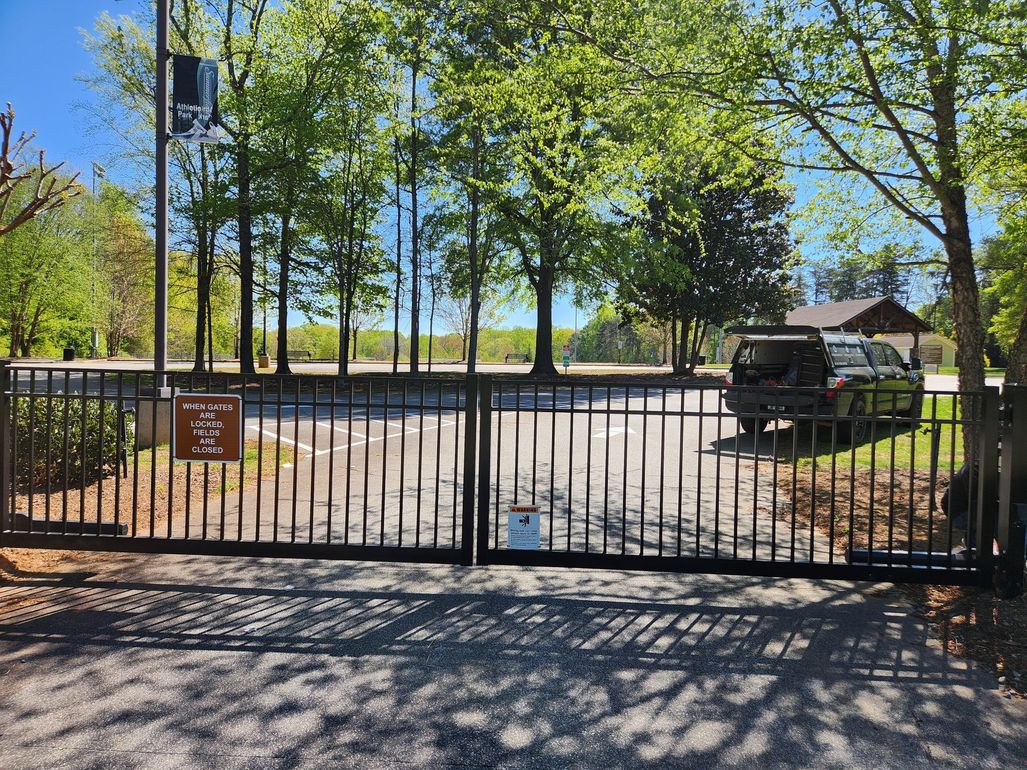 Black metal gate to a tree-lined park entrance on a sunny day