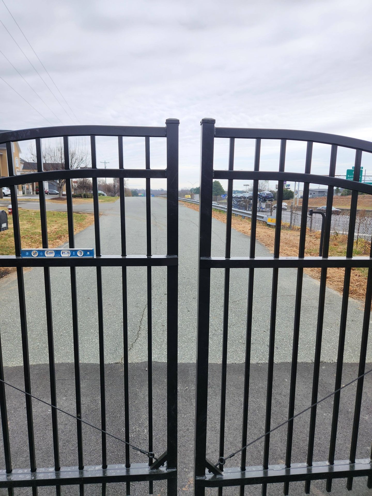 Black metal gate opening onto a gravel path and cloudy outdoor area.