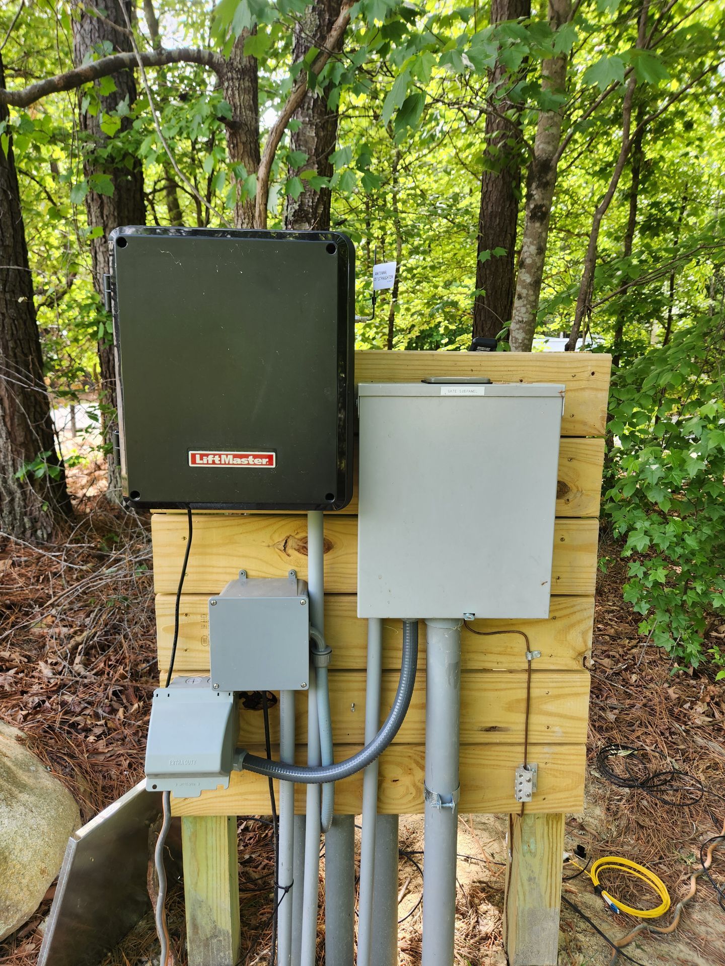 Outdoor electrical control boxes mounted on wooden posts in a wooded area.