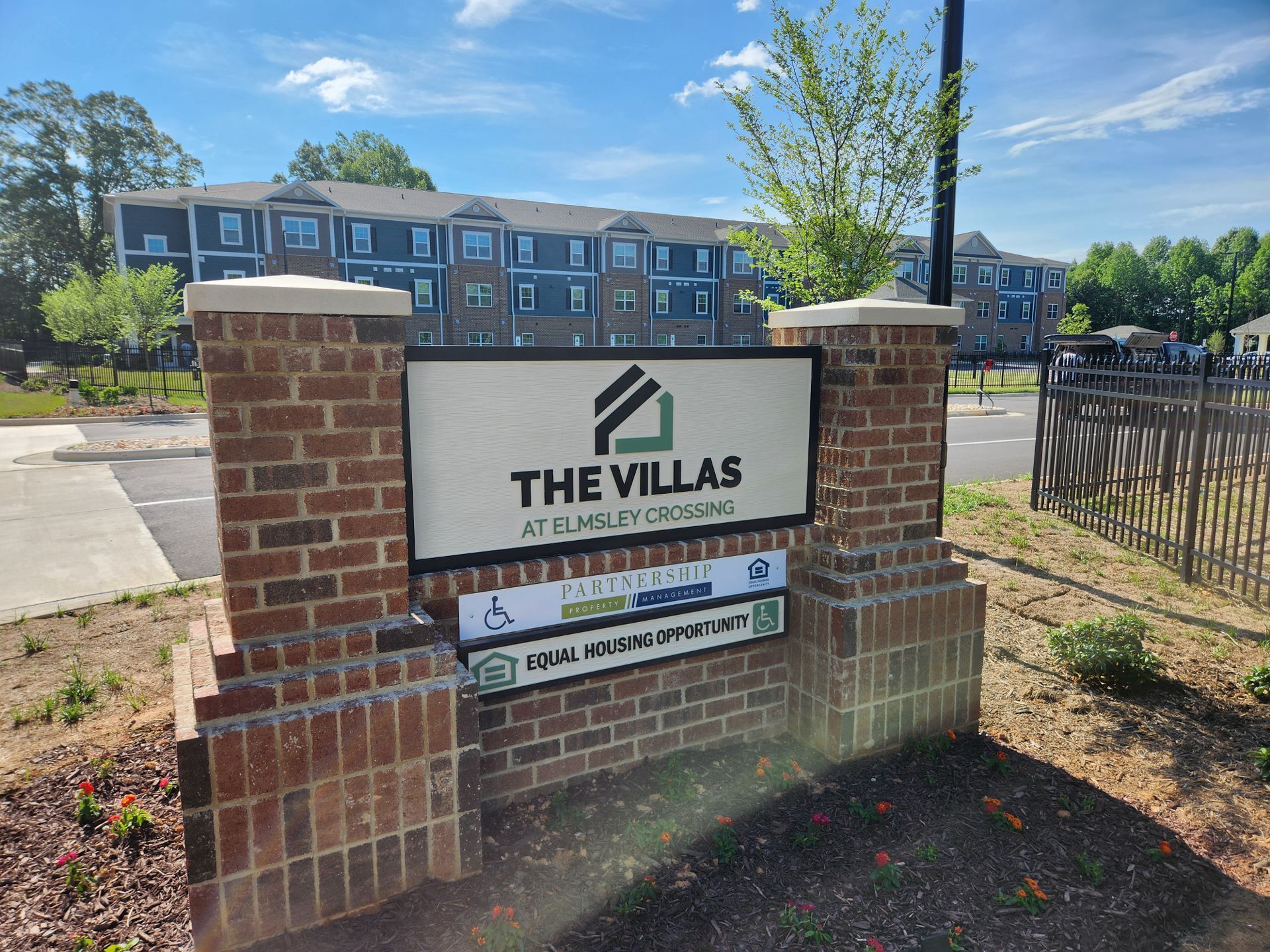 Brick entrance sign for The Villas apartment community with buildings and parking lot behind it