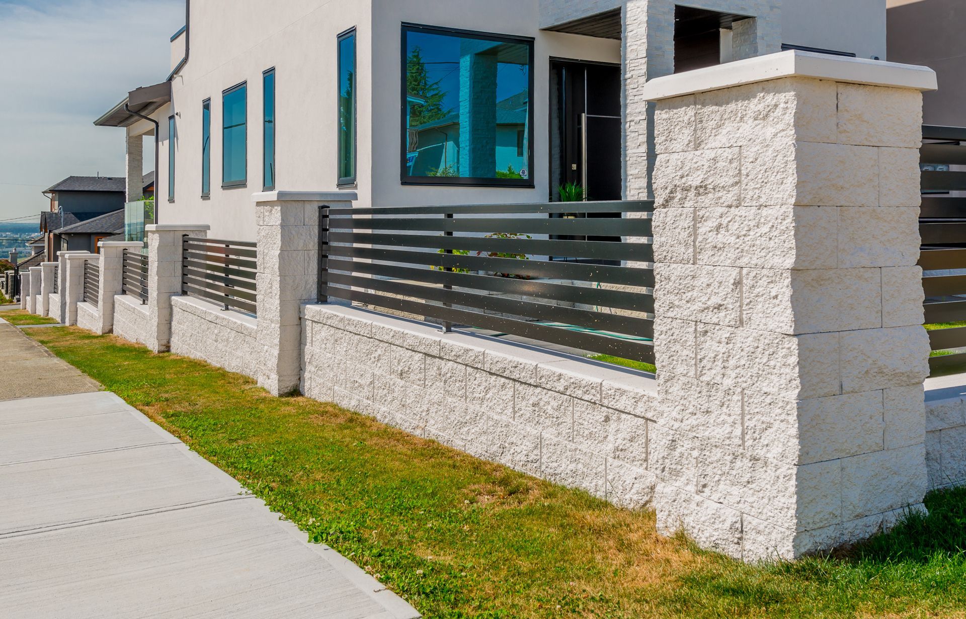 Modern white house with stone fence, dark metal gate, and sidewalk along the street