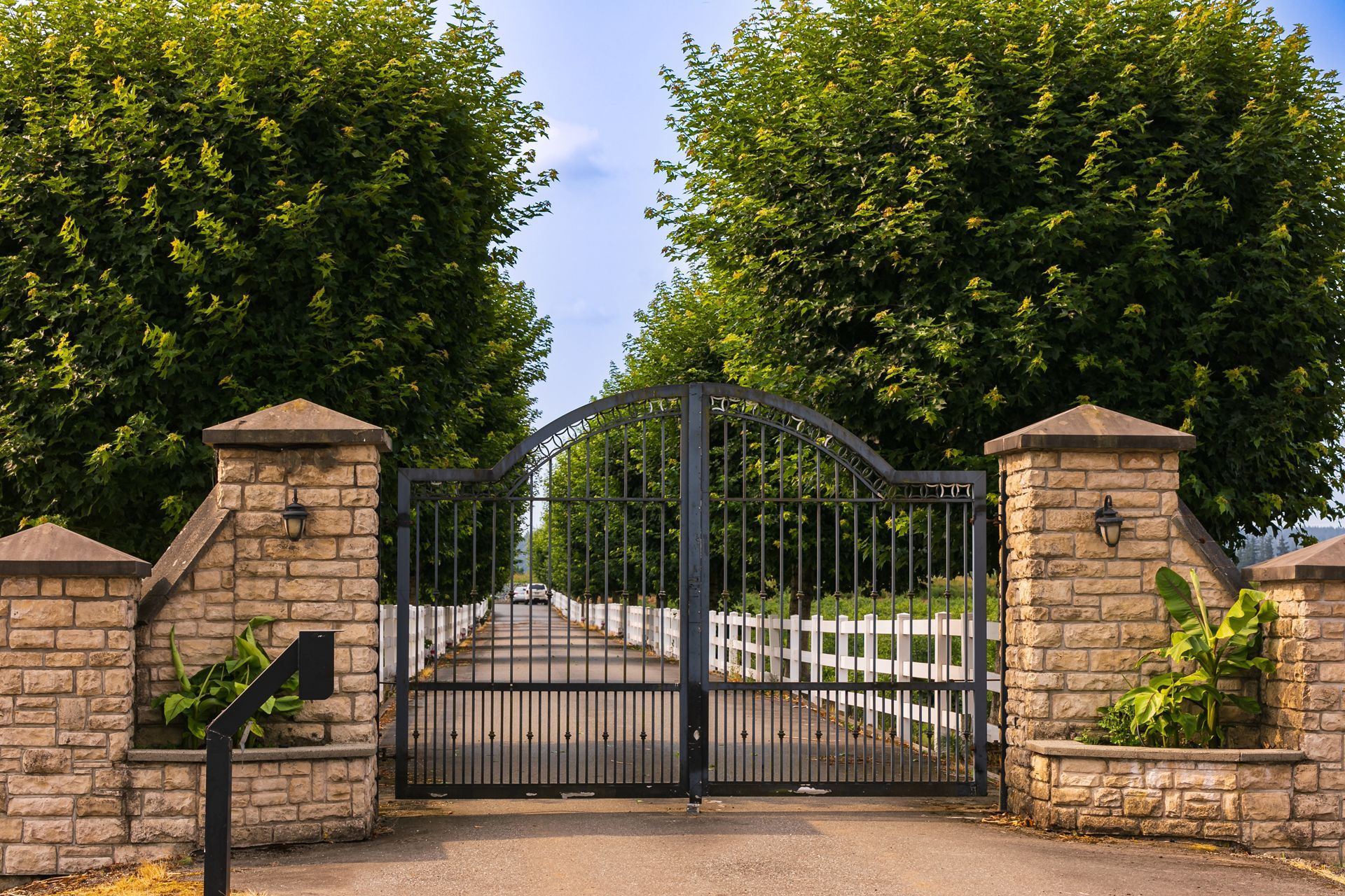 Stone entrance gate with black iron gates and tall green trees behind it