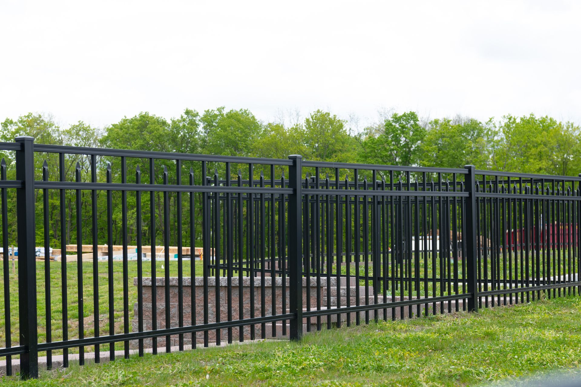 Black metal fence along a grassy roadside with trees in the background