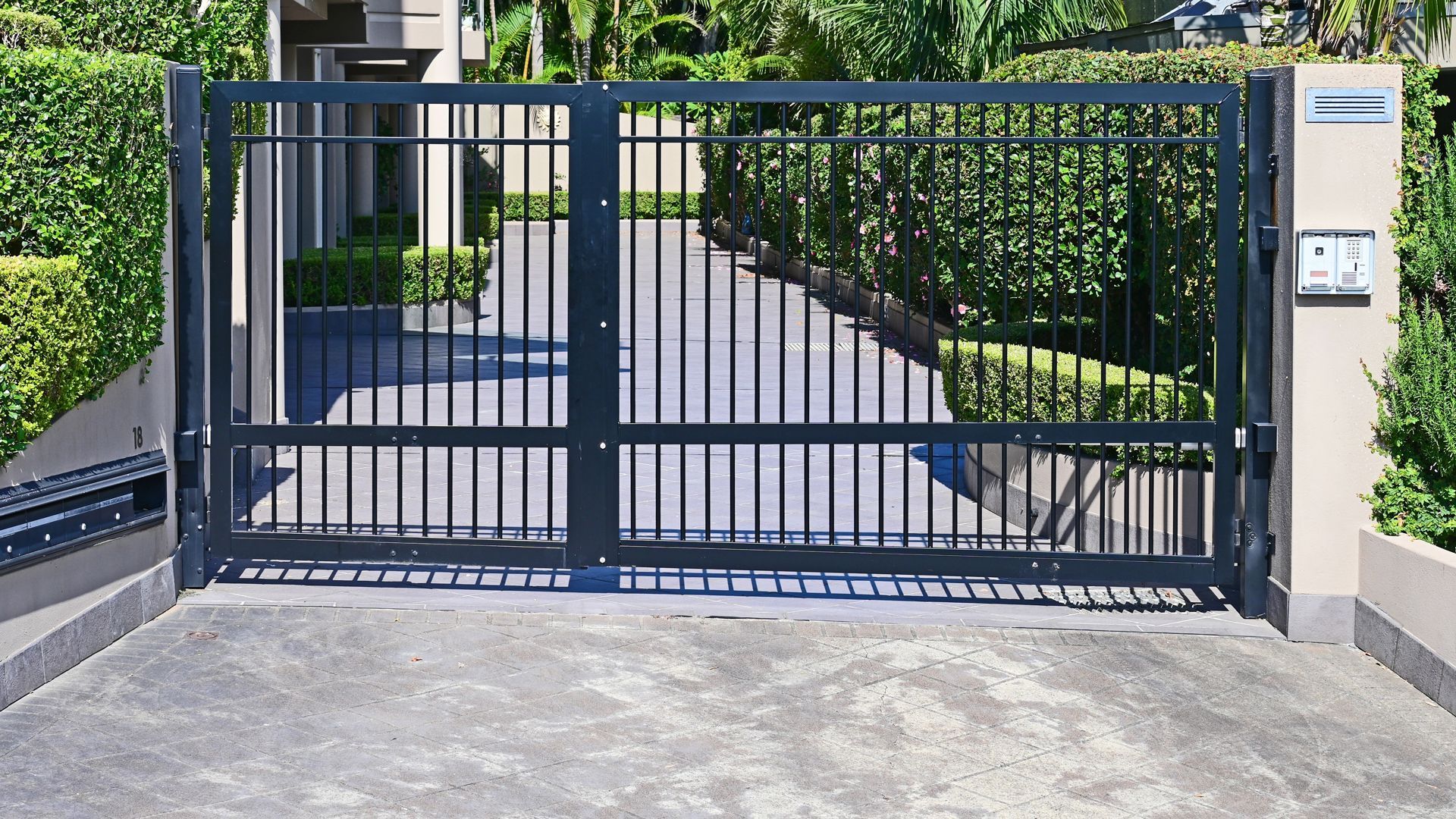 Blue metal driveway gate with a pedestrian door, opening to a tree-lined path and house entrance
