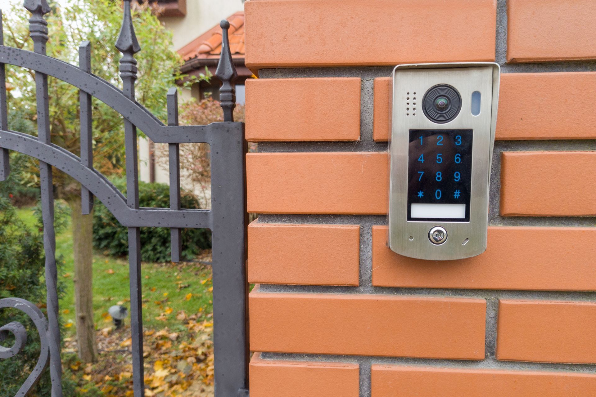 Keypad intercom mounted on a brick pillar beside a metal gate