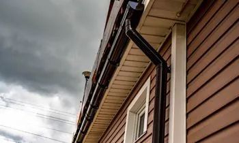Brown siding with black gutters on a house under a cloudy sky.