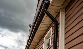 A brown house with a black gutter on the side of it.