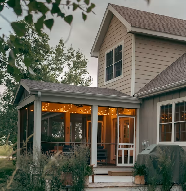 Cozy beige house porch with warm string lights and screened-in seating at dusk