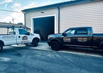 Two work trucks parked outside a tan building; white truck, left; black truck, right; both with business logos.