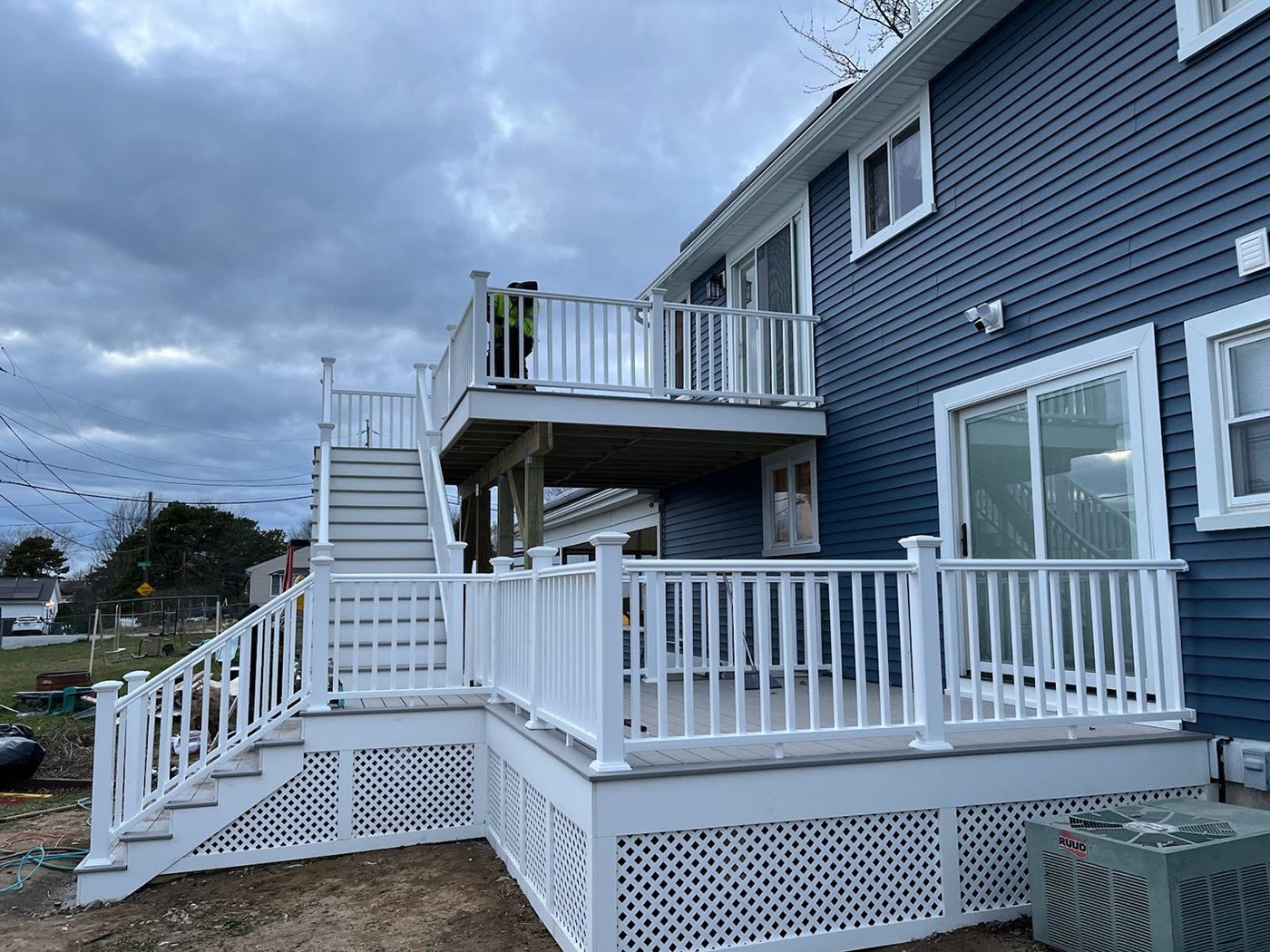 Two-story white deck attached to a blue house with stairs. Overcast sky.