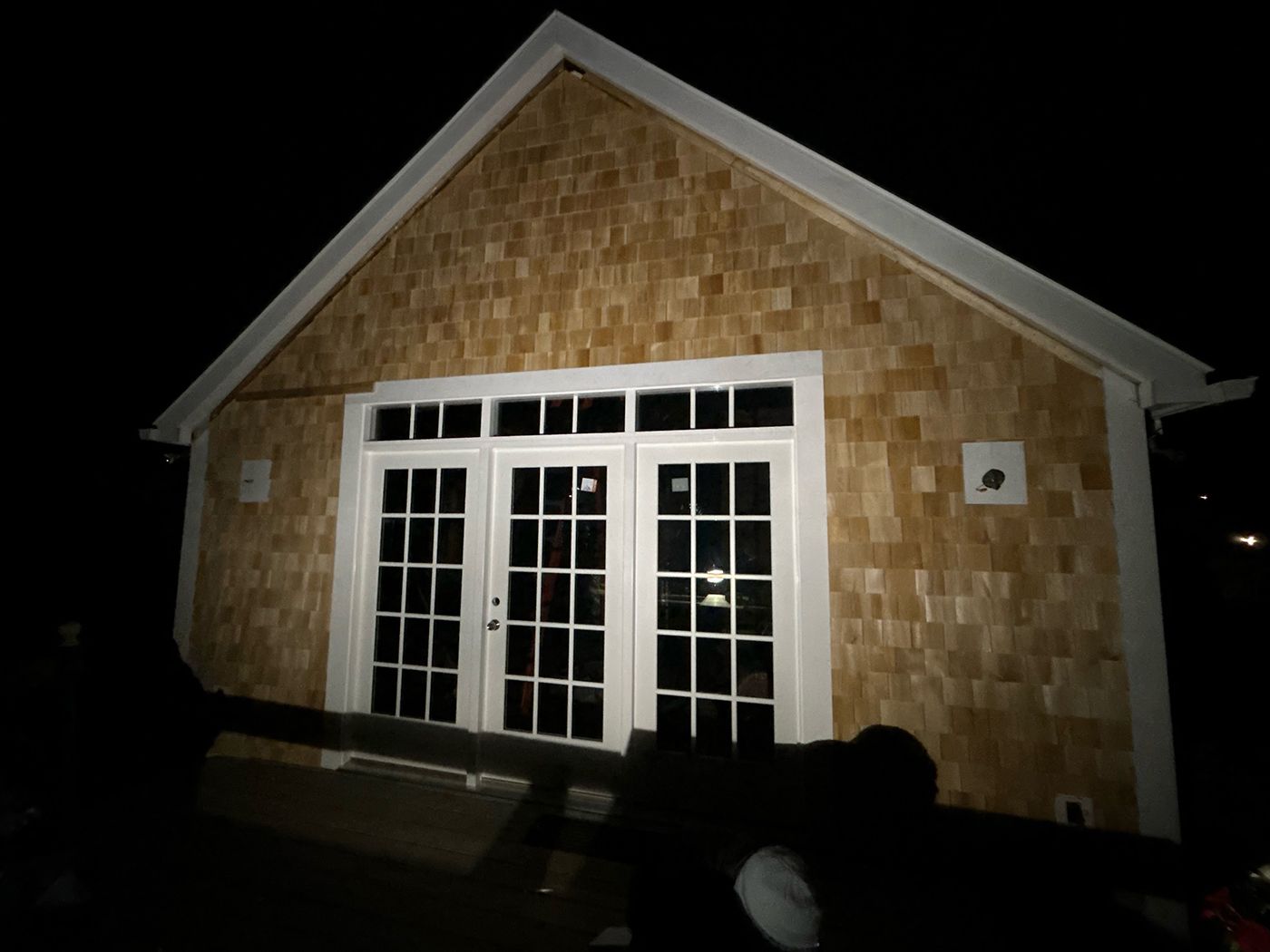 Exterior of a building at night. Cedar shingle siding with white-framed French doors.
