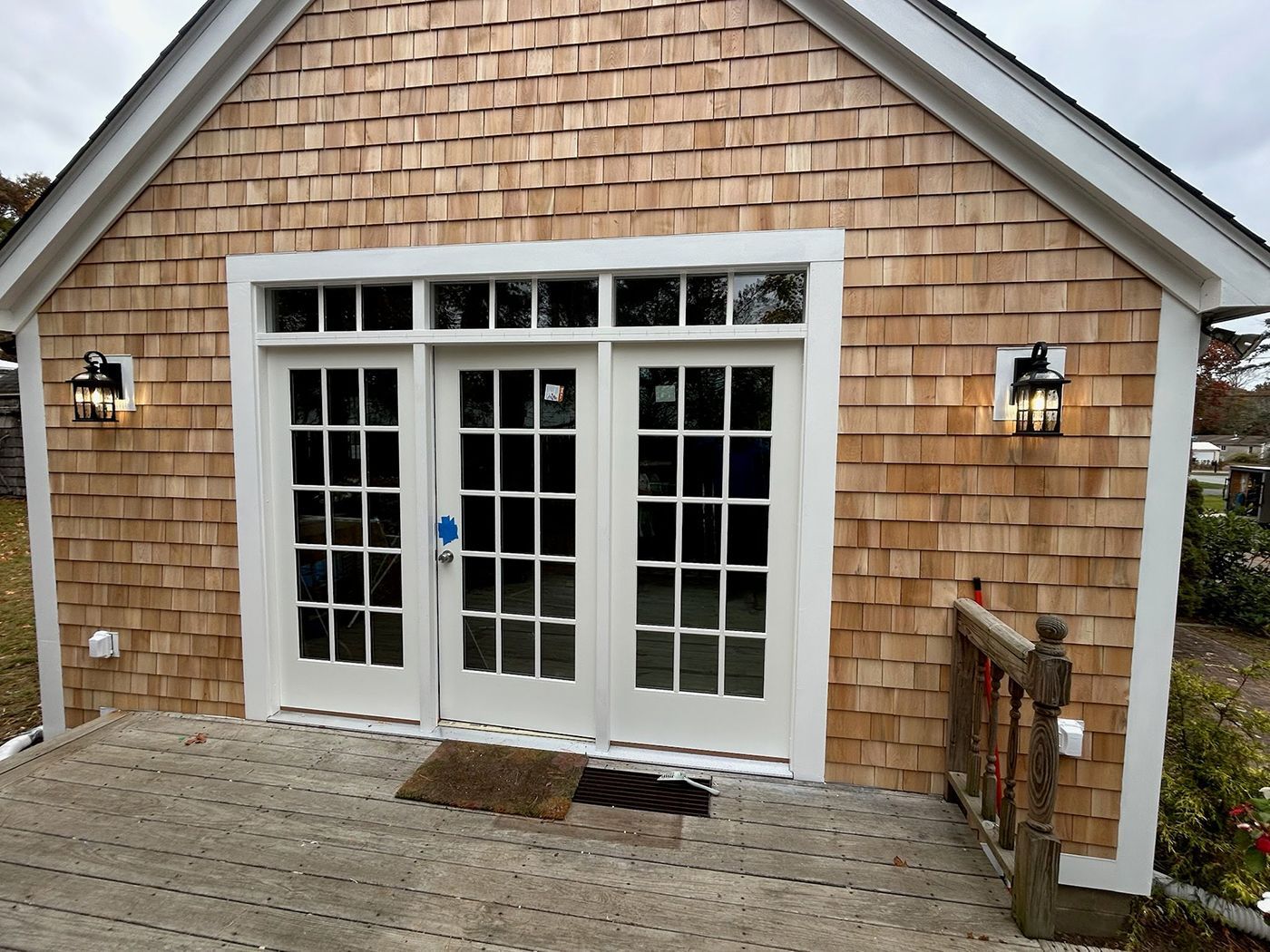 Building exterior with wood shake siding, white French doors, and sconce lights.