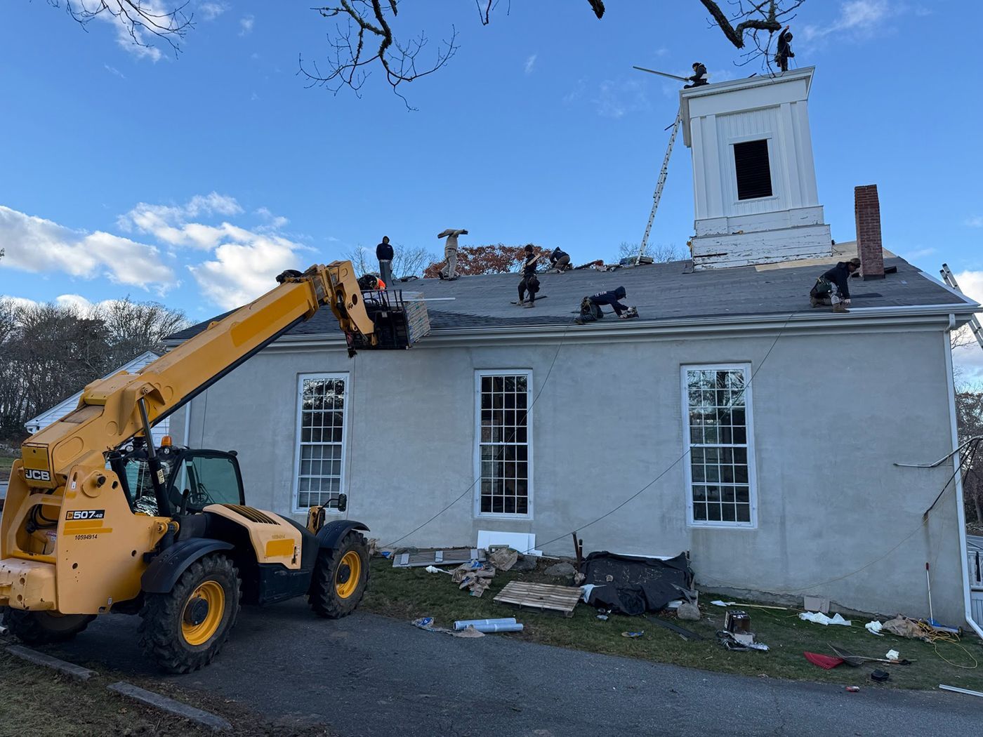 A yellow forklift removing bricks from a church roof with workers in action under a blue sky.