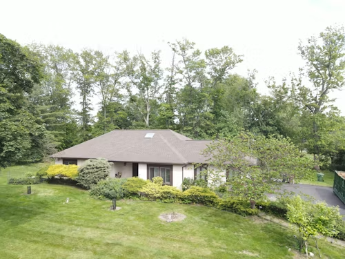 Single-story house with gray roof, surrounded by green lawn and trees