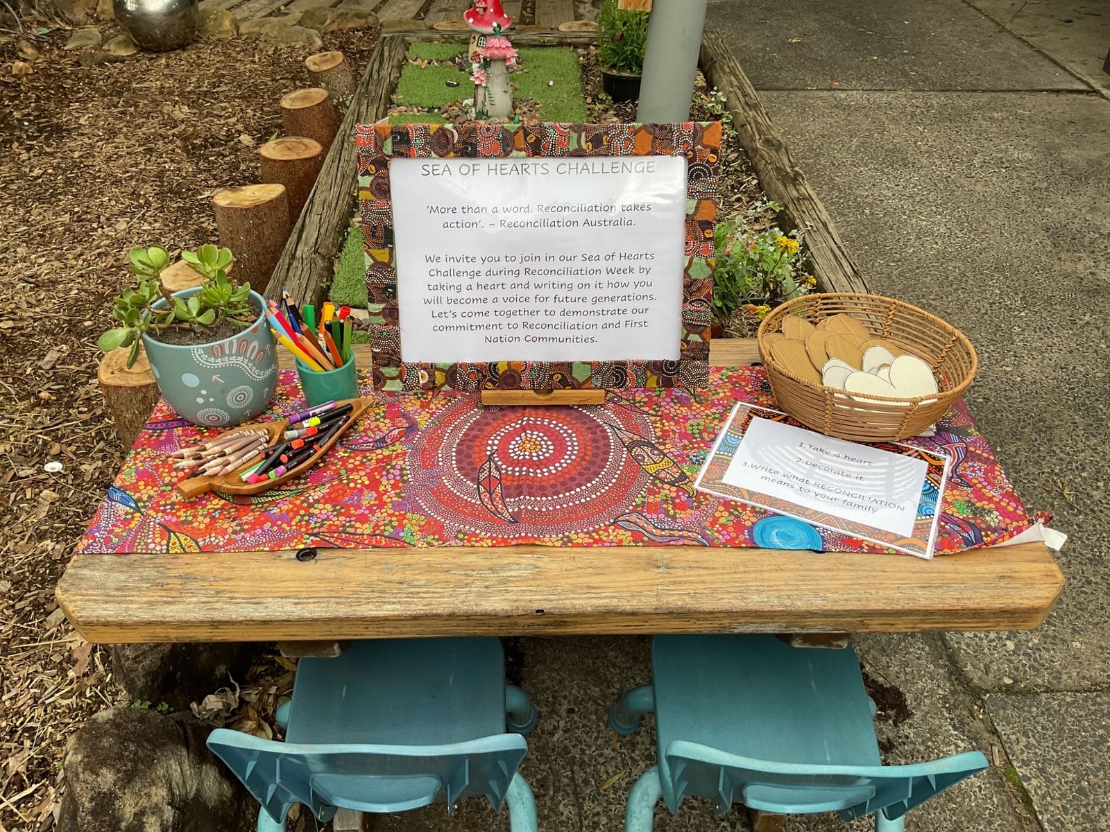 A decorated table with a sign, art supplies, cookies, and two blue chairs outdoors. — Kinburra Preschool (Kincumber) in Kincumber, NSW