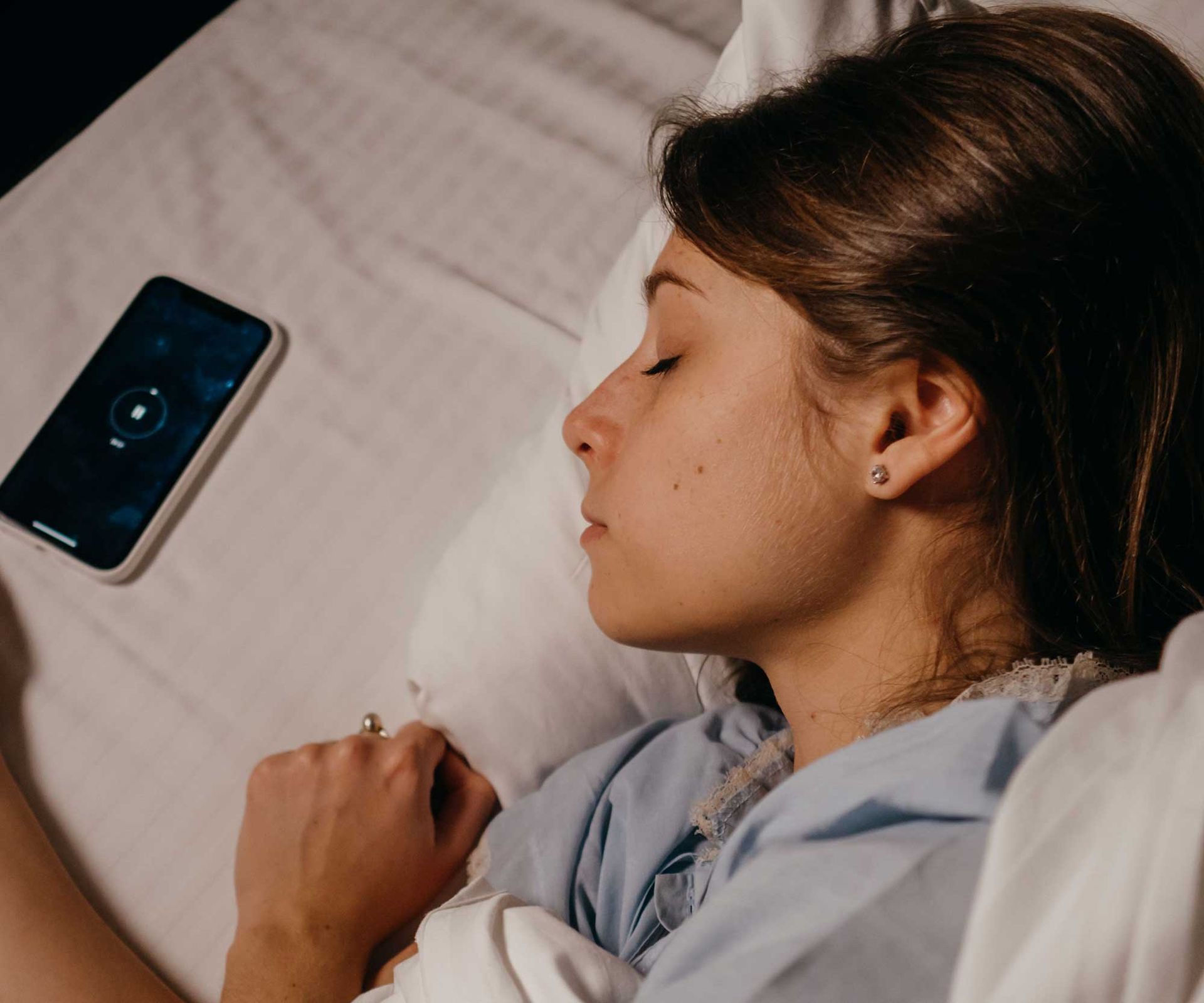Woman sleeping in bed with a smartphone glowing beside her on the pillow