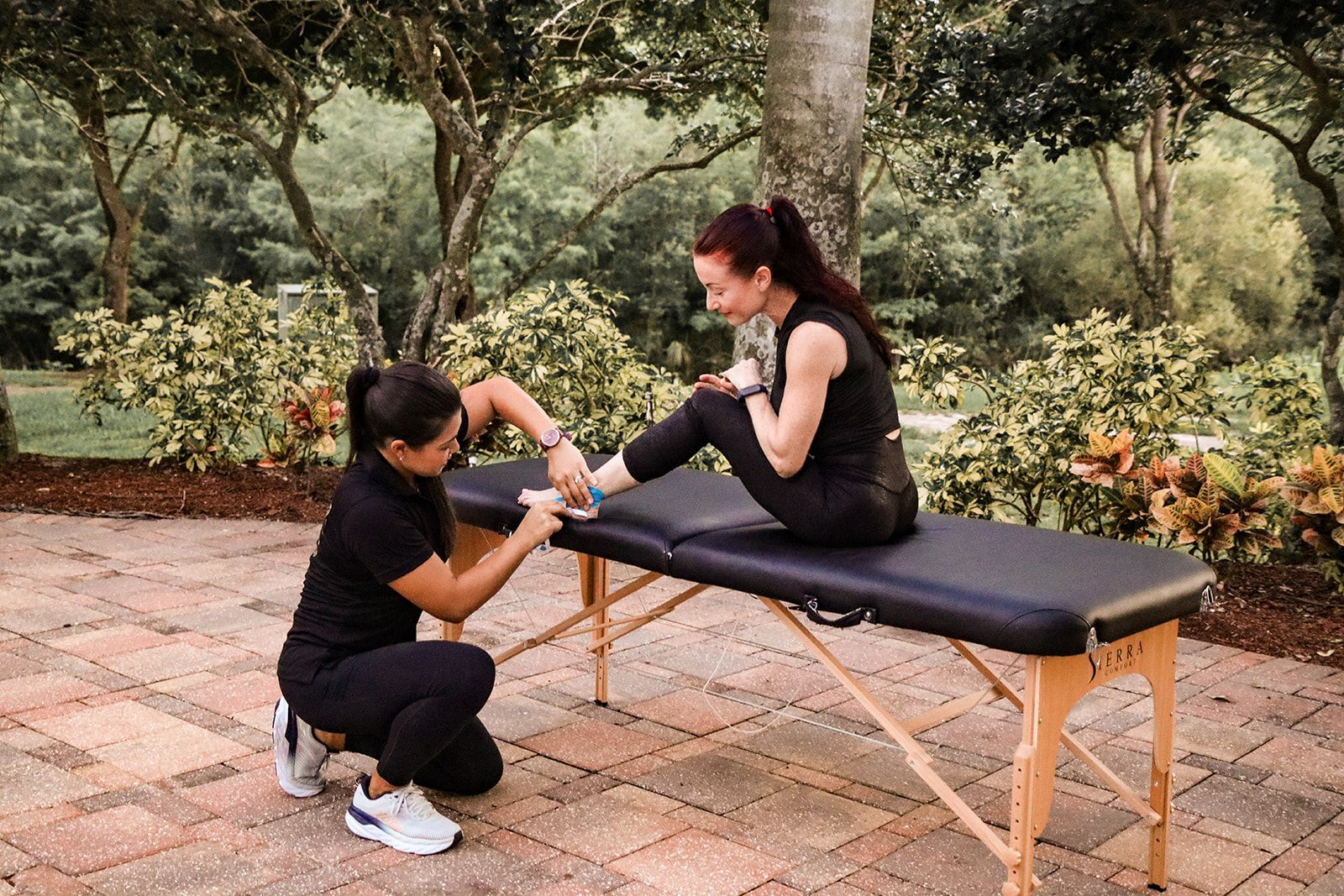 A woman is kneeling down next to a woman sitting on a table.