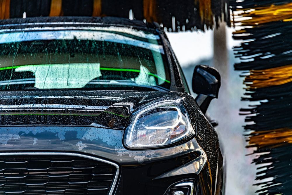 A dark car being washed by automated rotating brushes in a car wash.