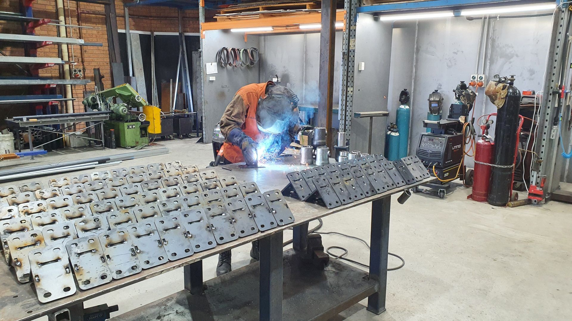 A Welder Works at A Workbench in A Metal Shop Surrounded by Numerous Metal plates — Real Engineering in West Gosford, NSW