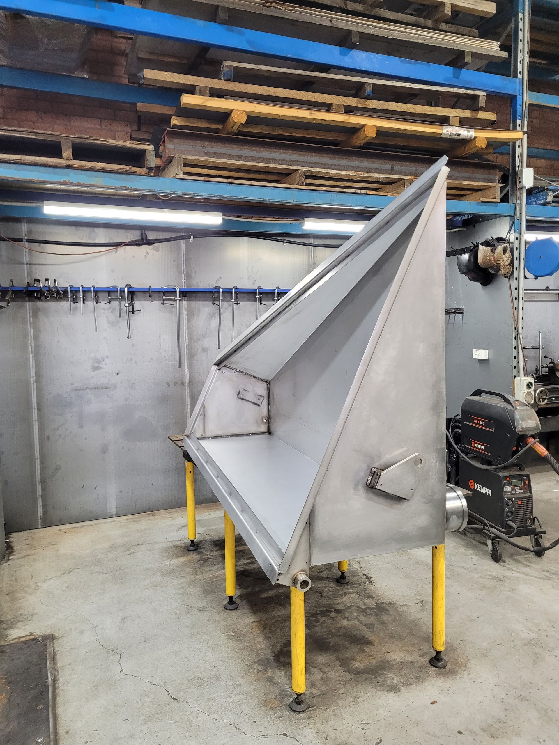 A Stainless Steel, Wedge-Shaped Industrial Hopper with Yellow Legs — Real Engineering in West Gosford, NSW