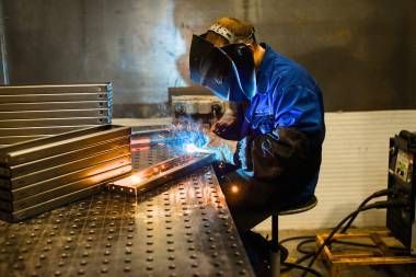 A Man Wearing A Welding Helmet Is Grinding A Piece Of Metal In A Factory — Real Engineering in Seven Hills, NSW