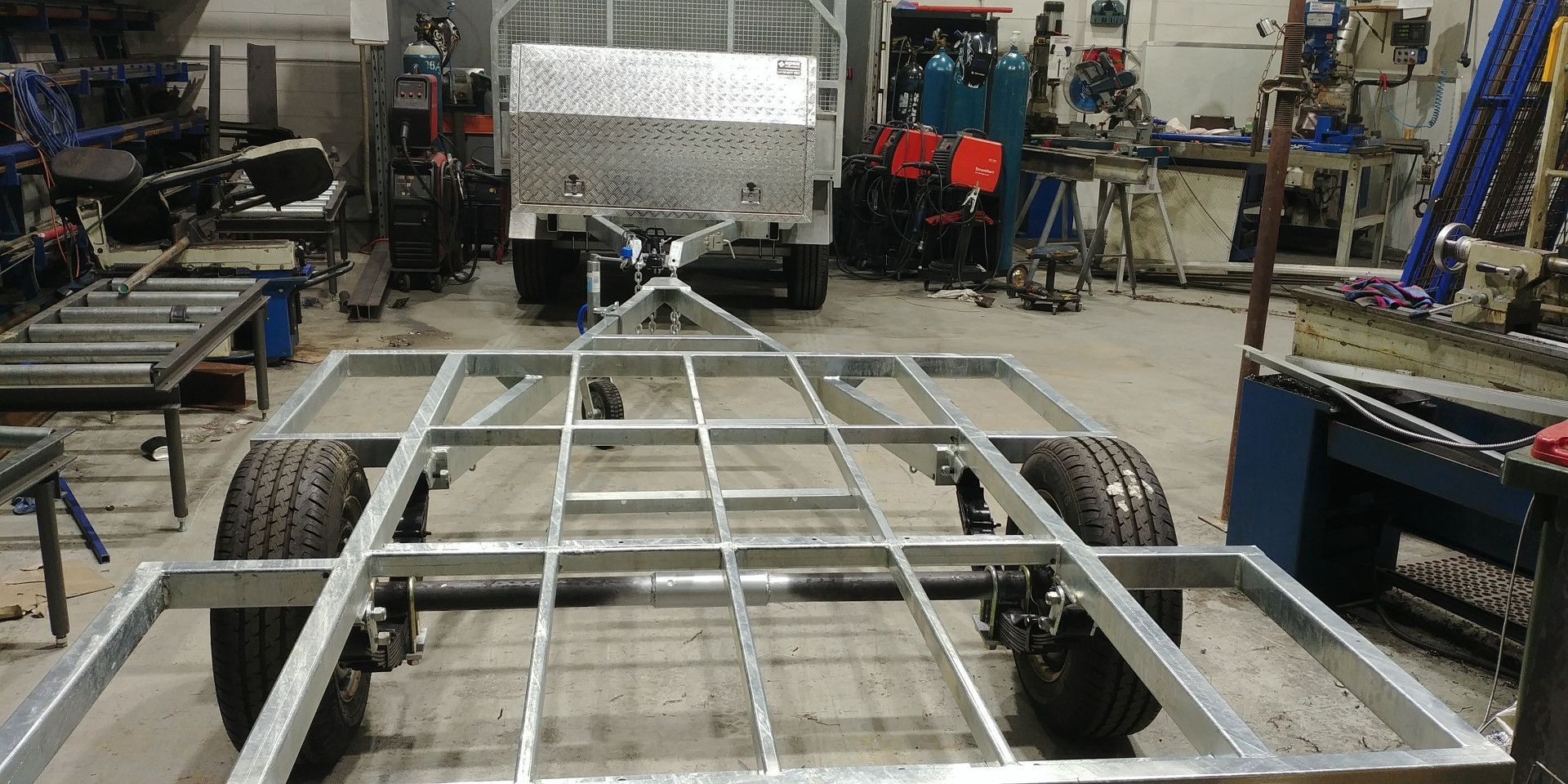 A Metal Trailer Chassis Sits in A Workshop, with A Completed Trailer — Real Engineering in West Gosford, NSW