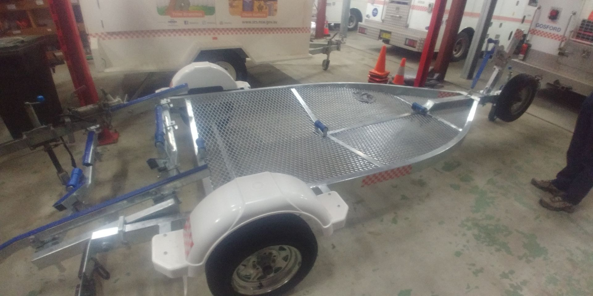 A metal utility trailer with white fenders and a diamond-plate deck, parked inside a garage.
