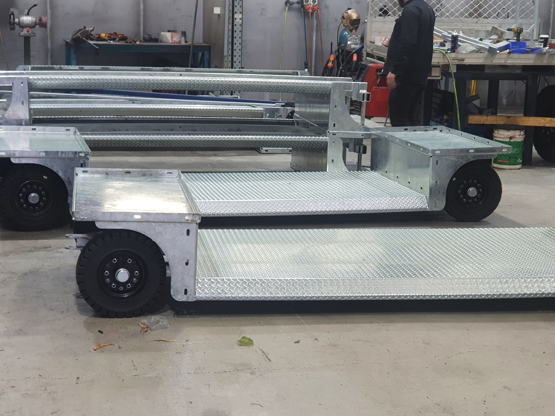 Two industrial, diamond-plate steel flatbed trailers with black wheels sit in a workshop.