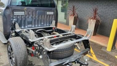 A dark grey pickup truck with its cargo bed removed, exposing the chassis, spare tire, and rear suspension system.