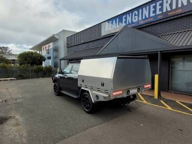 A black pickup truck with a silver metal canopy parked in front of a building labelled Real Engineering.