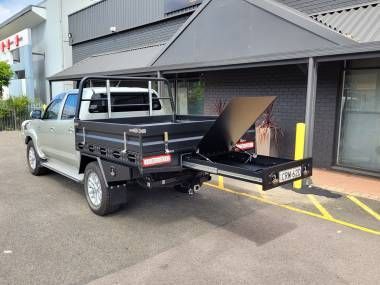 A silver utility truck with an open tray, featuring an extended sliding metal storage drawer parked outside a building.